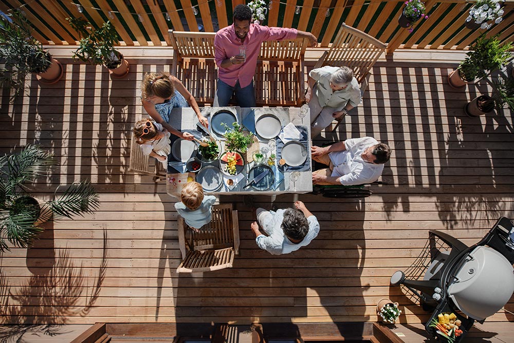 Top view of 3 generations family eating at barbecue party dinner on patio, people sitting at table on patio with grill.